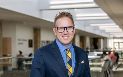 Law Dean smiles in a suit with a patterned tie, inside a modern building.