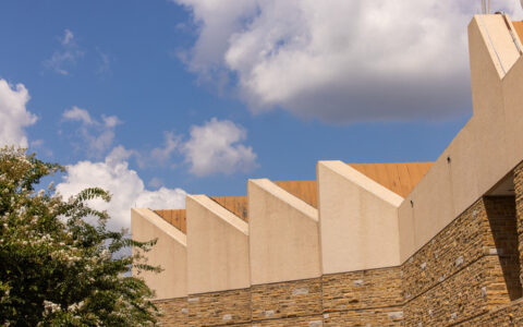 Building exterior with sawtooth roof design and stone facade under a blue sky.