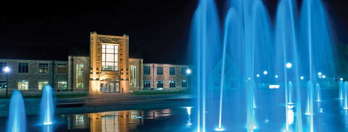 The fountains of Chapman Commons glowing blue in front of Collins Hall at night