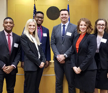 Law students in professional attire, possibly from the College of Law, standing in front of a courtroom backdrop.