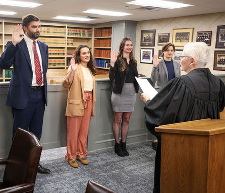 College of Law students being sworn in by a judge, raising their right hands.
