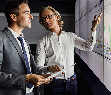 Photograph of two men discussing a graph projected on a screen in an office