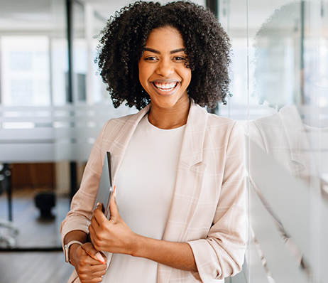 Photograph of a smiling woman holding a closed laptop in an office setting