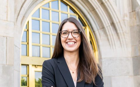 Professional woman with glasses smiles in front of McFarlin Library entrance.